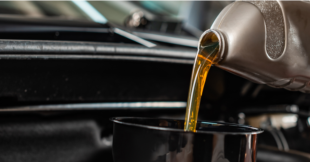 Oil being poured from a silver container into a black container in an engine bay.