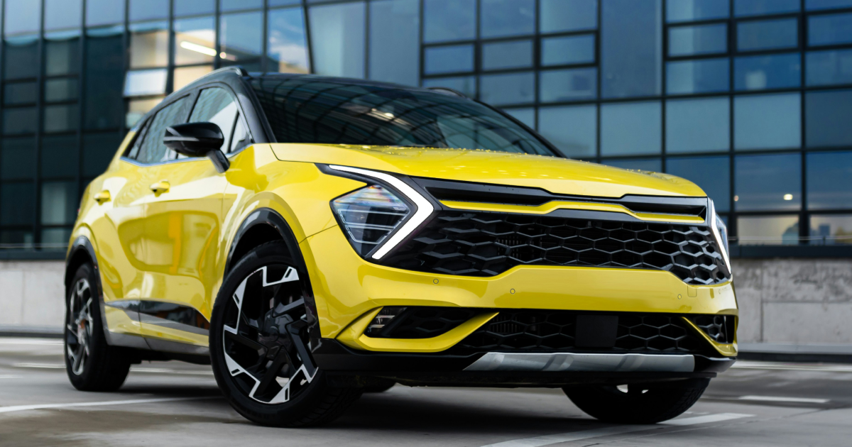 Yellow Kia Sportage SUV parked in front of a modern building with a black roof and black wheels.