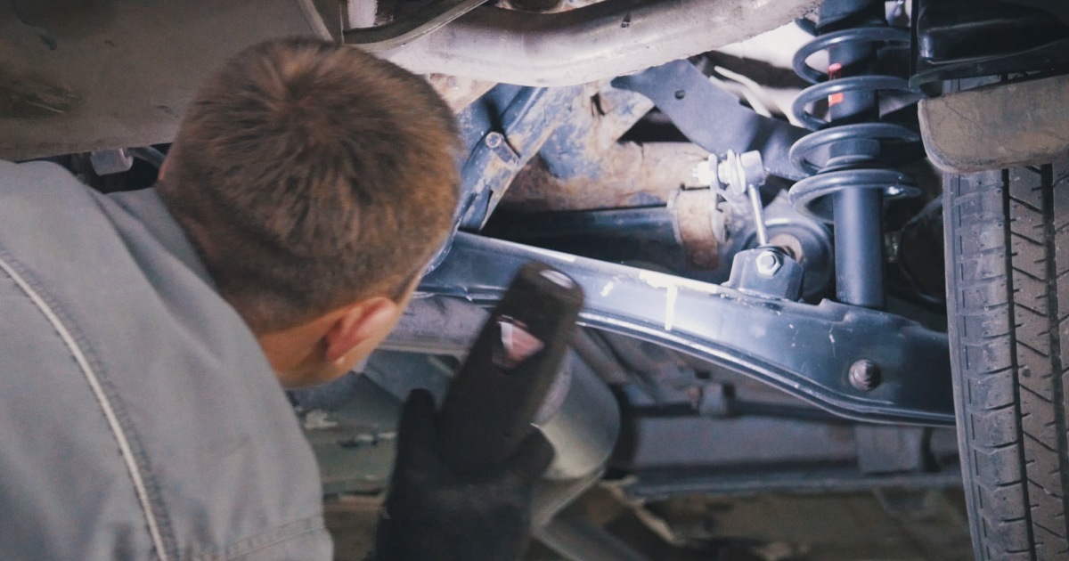 Mechanic examines undercarriage of a vehicle with a flashlight, looking for damage.