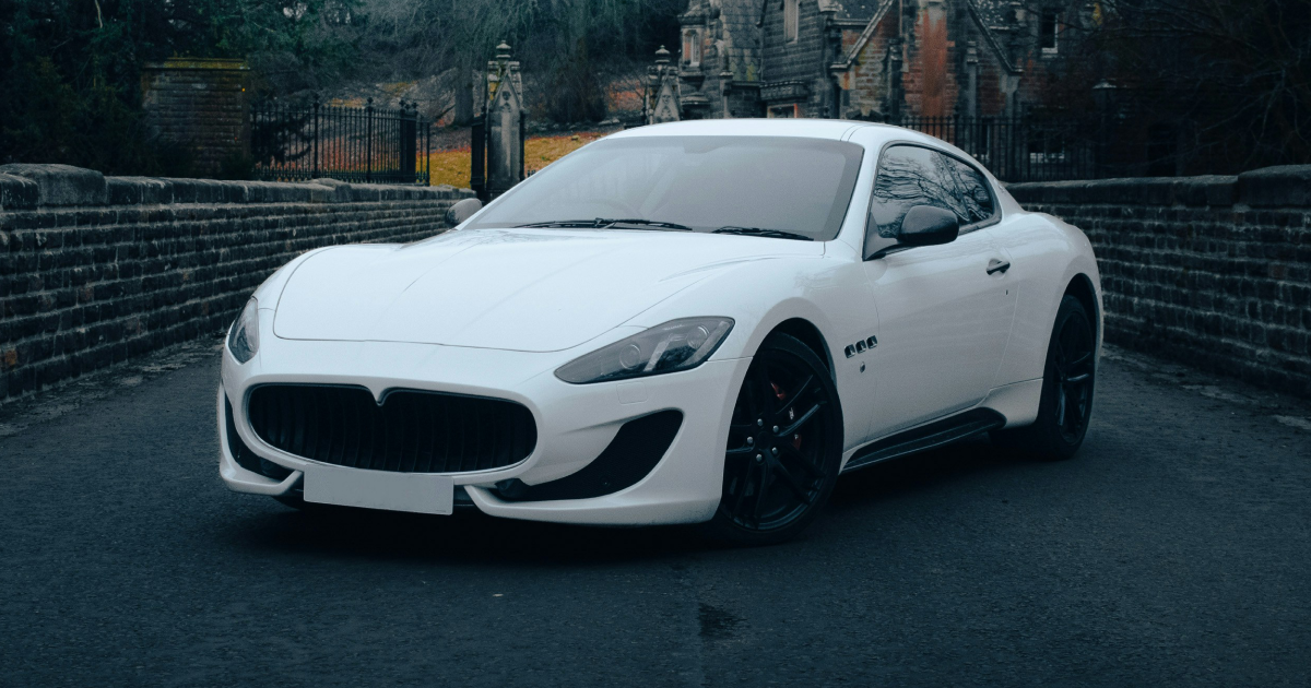 White Maserati GranTurismo coupe on a bridge with buildings in the background.