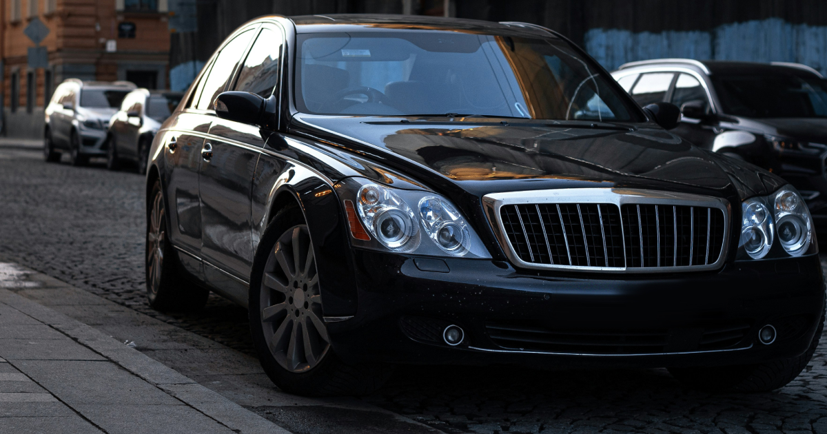 Black Maybach luxury car parked on a cobblestone street in a city.