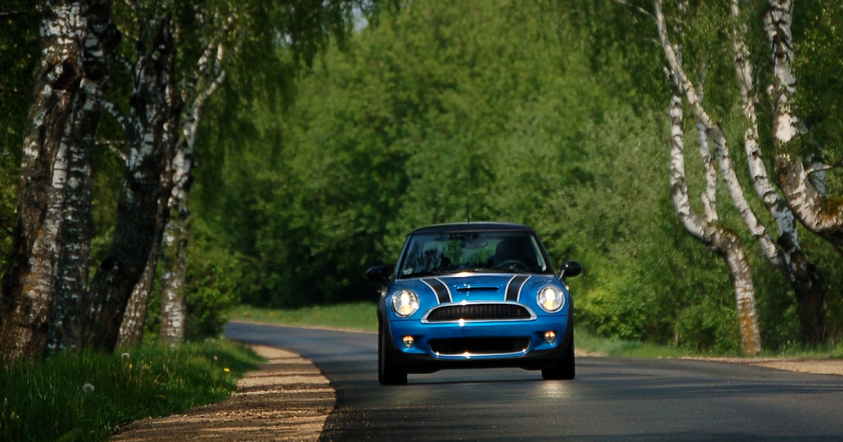 Blue Mini Cooper driving on a tree-lined road.
