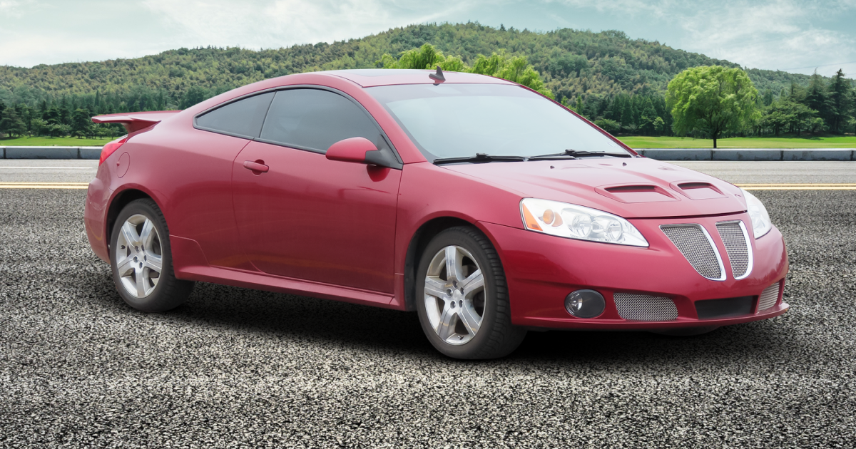 Red Pontiac G6 coupe with spoiler, on a road, mountains in the background.