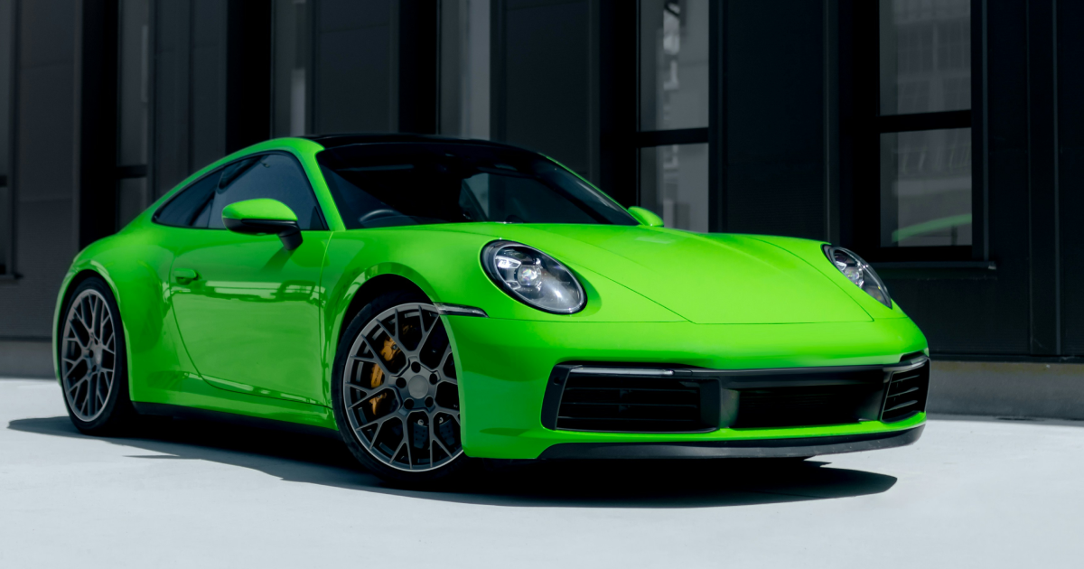 Green Porsche sports car parked in front of a modern building.