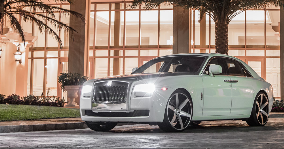White Rolls Royce coupe parked in front of a lit building at night, with large black and silver rims.