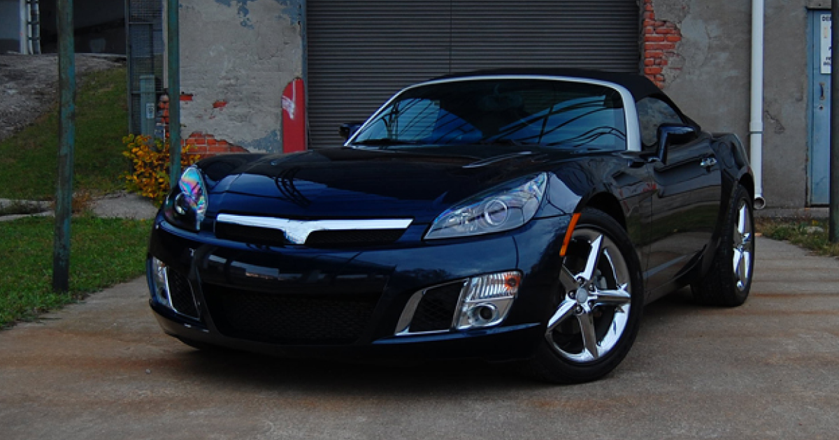 Dark blue Saturn Sky convertible parked in front of a brick building, sunny day.