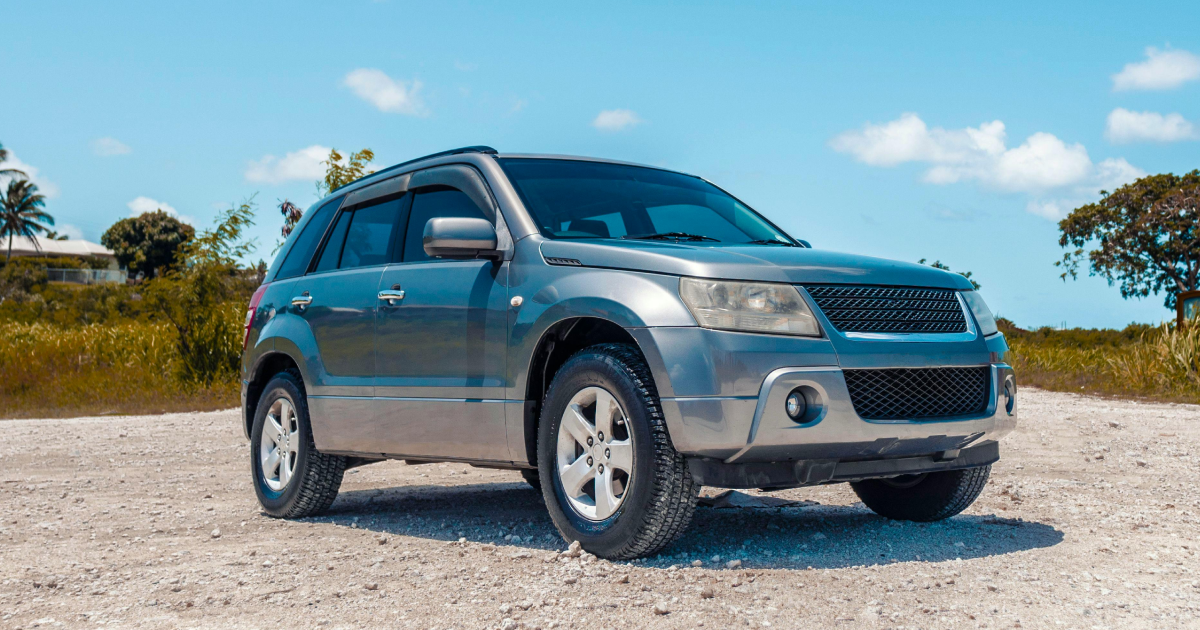 Silver SUV on a dirt road with blue sky and trees in the background.