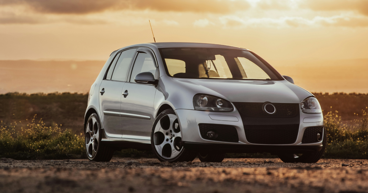 Silver Volkswagen Golf GTI parked on dirt road with a sunset in the background.