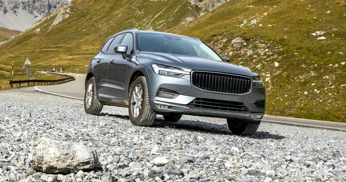 Gray Volvo SUV on a gravel road, mountains in background.