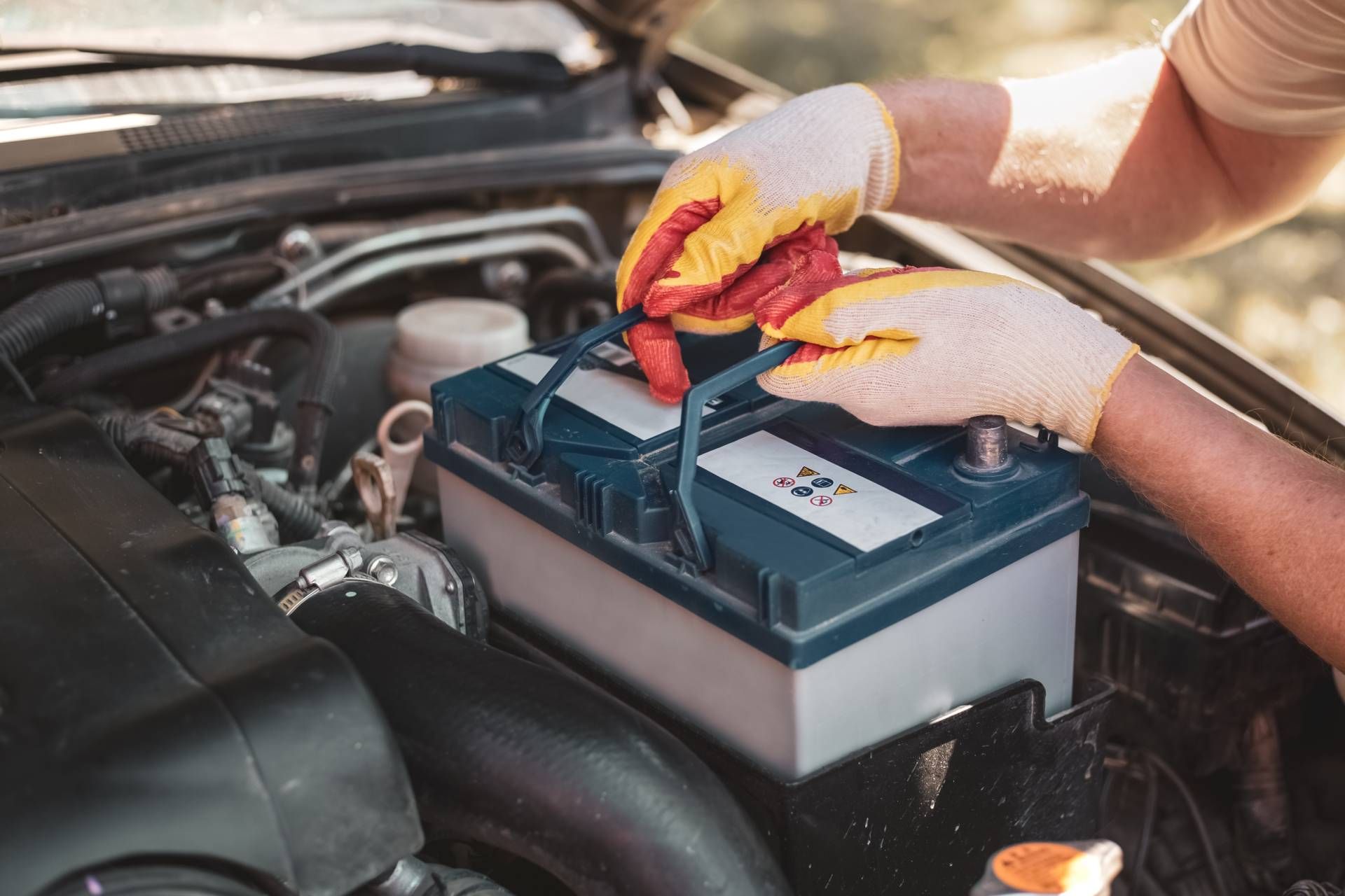 Hands in gloves securing a car battery in the engine bay.