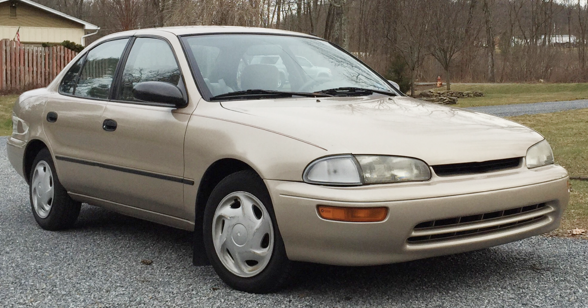 Tan 1990s Toyota Corolla sedan parked on gravel.