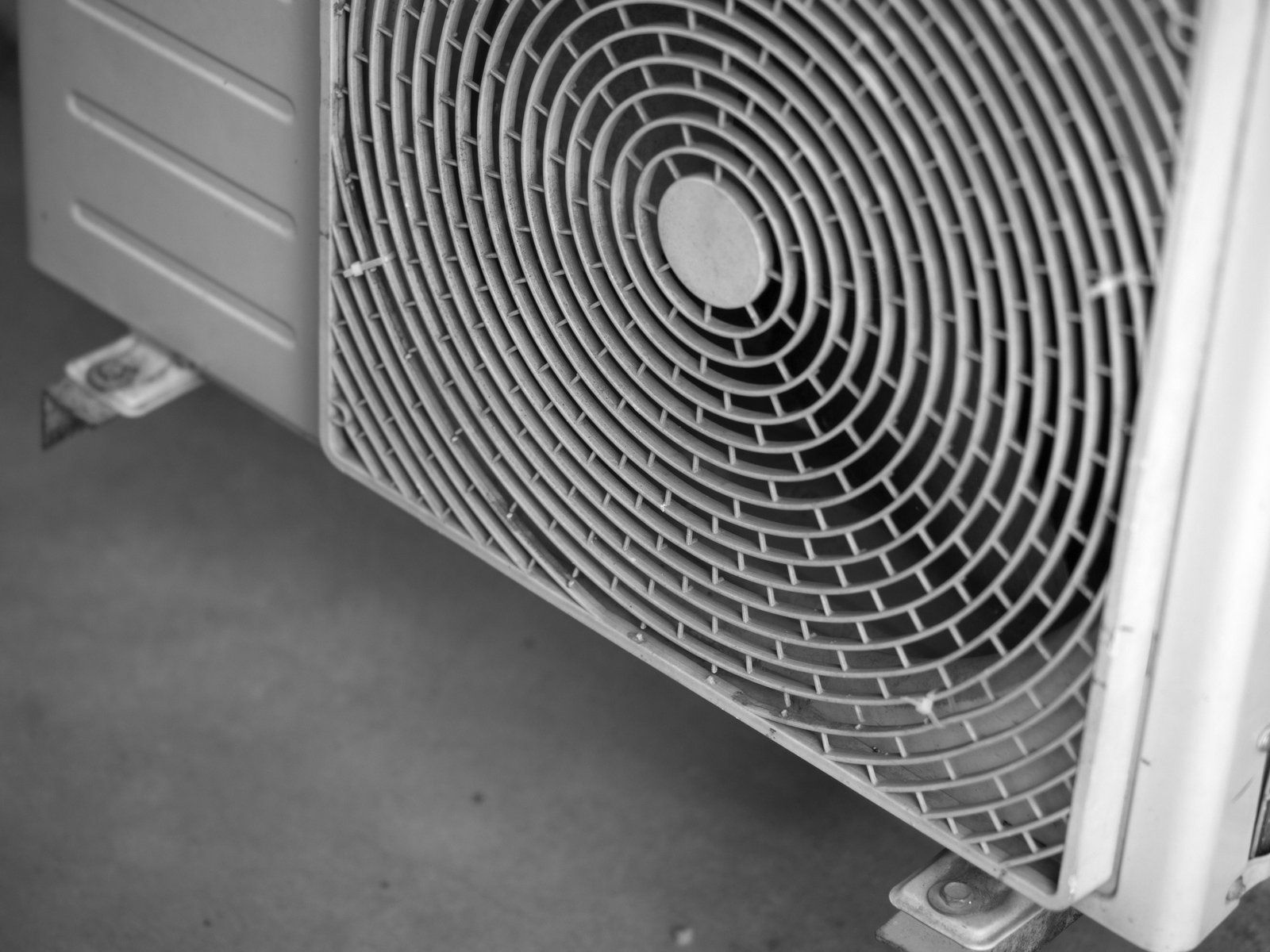 Air conditioning unit's fan with a spiral-shaped metal grille in gray and white, mounted outside.