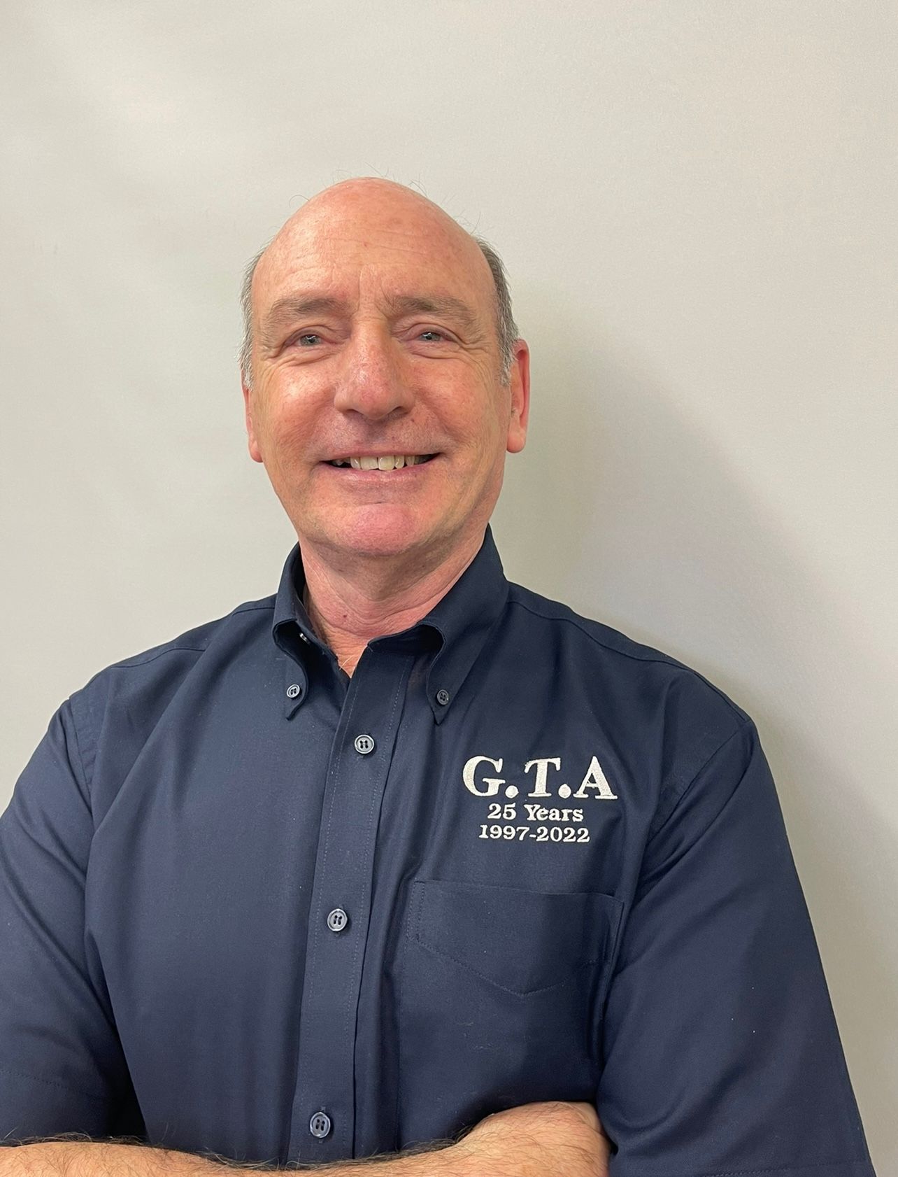 A man in a blue shirt is smiling with his arms crossed.