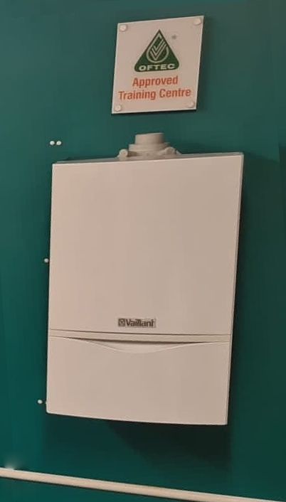 A white boiler is hanging on a green wall next to a sign that says approved training centre.