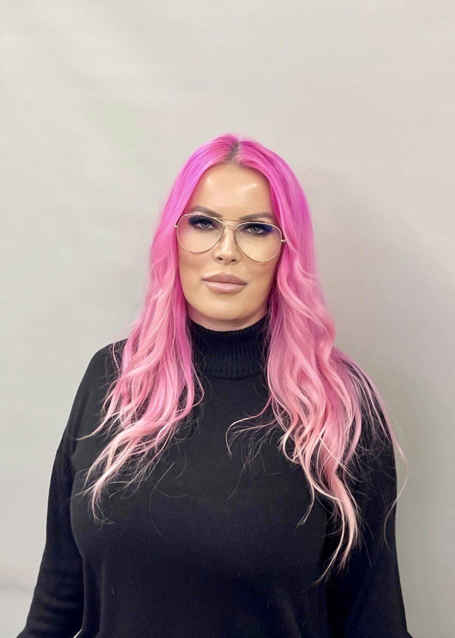 A woman with pink hair and glasses is wearing a black sweater.