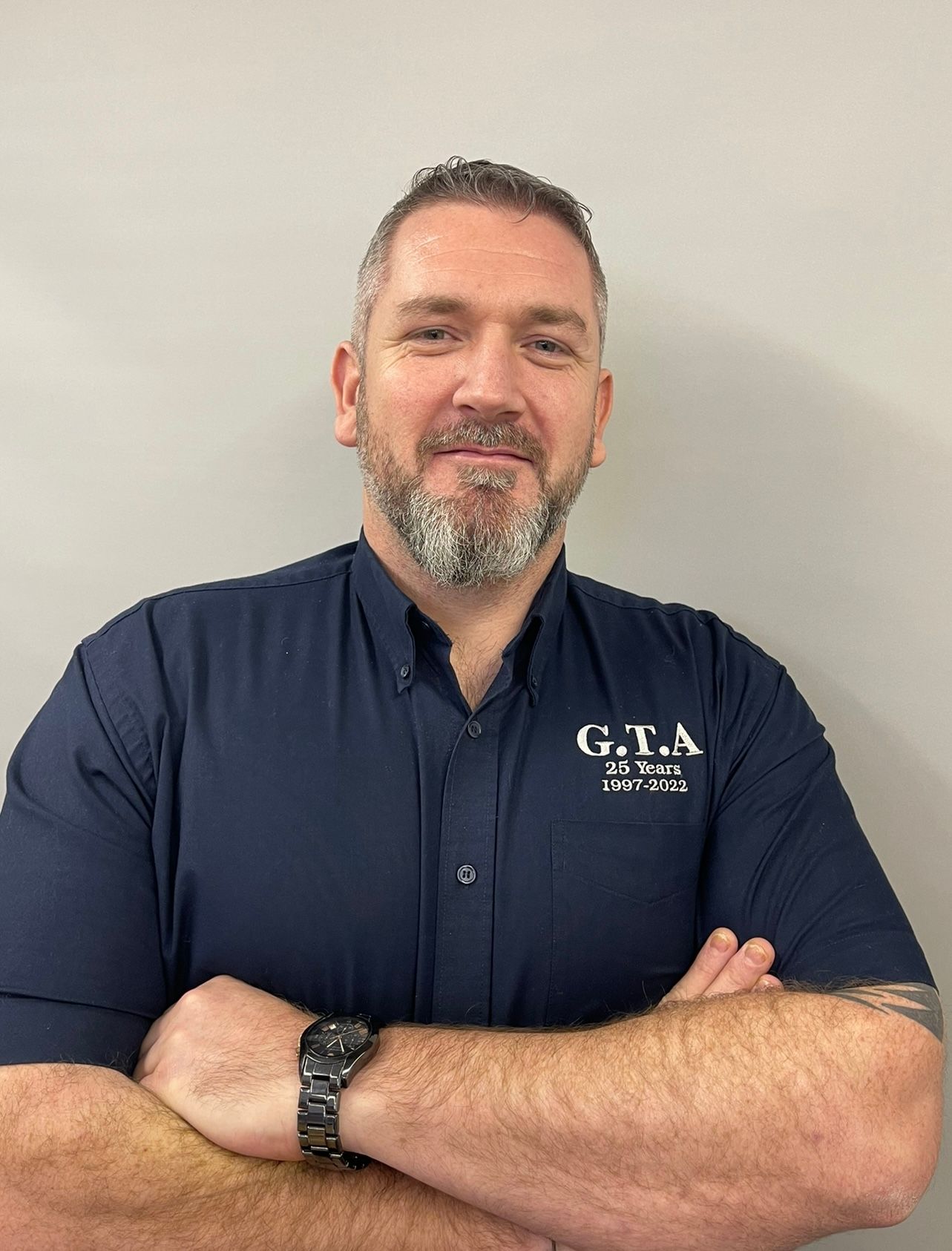 A man with a beard is wearing a blue shirt and a watch.