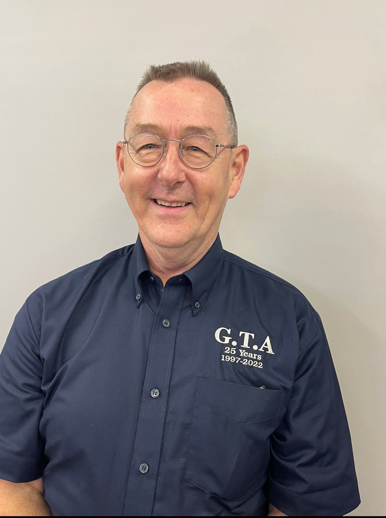 A man wearing glasses and a blue shirt is smiling for the camera.