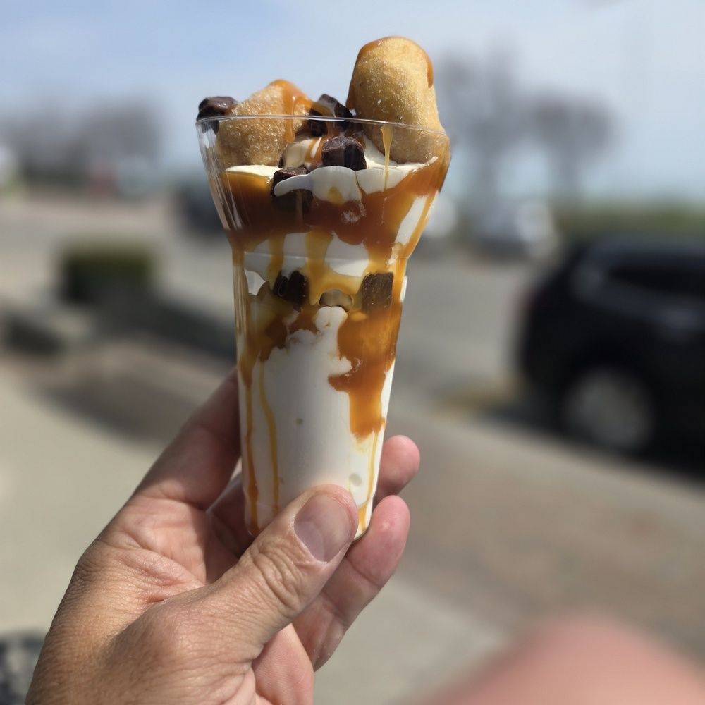 A person is holding a cup of ice cream with mini donuts on top.