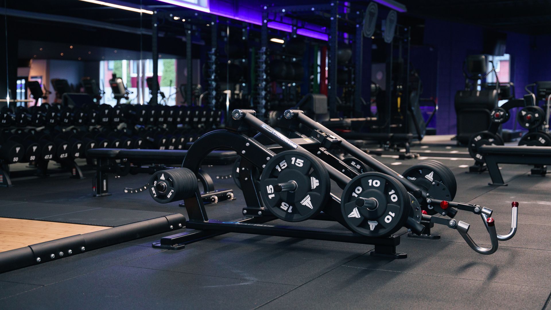 Gym equipment on a black floor, with sleds and weights in a dimly lit fitness center.