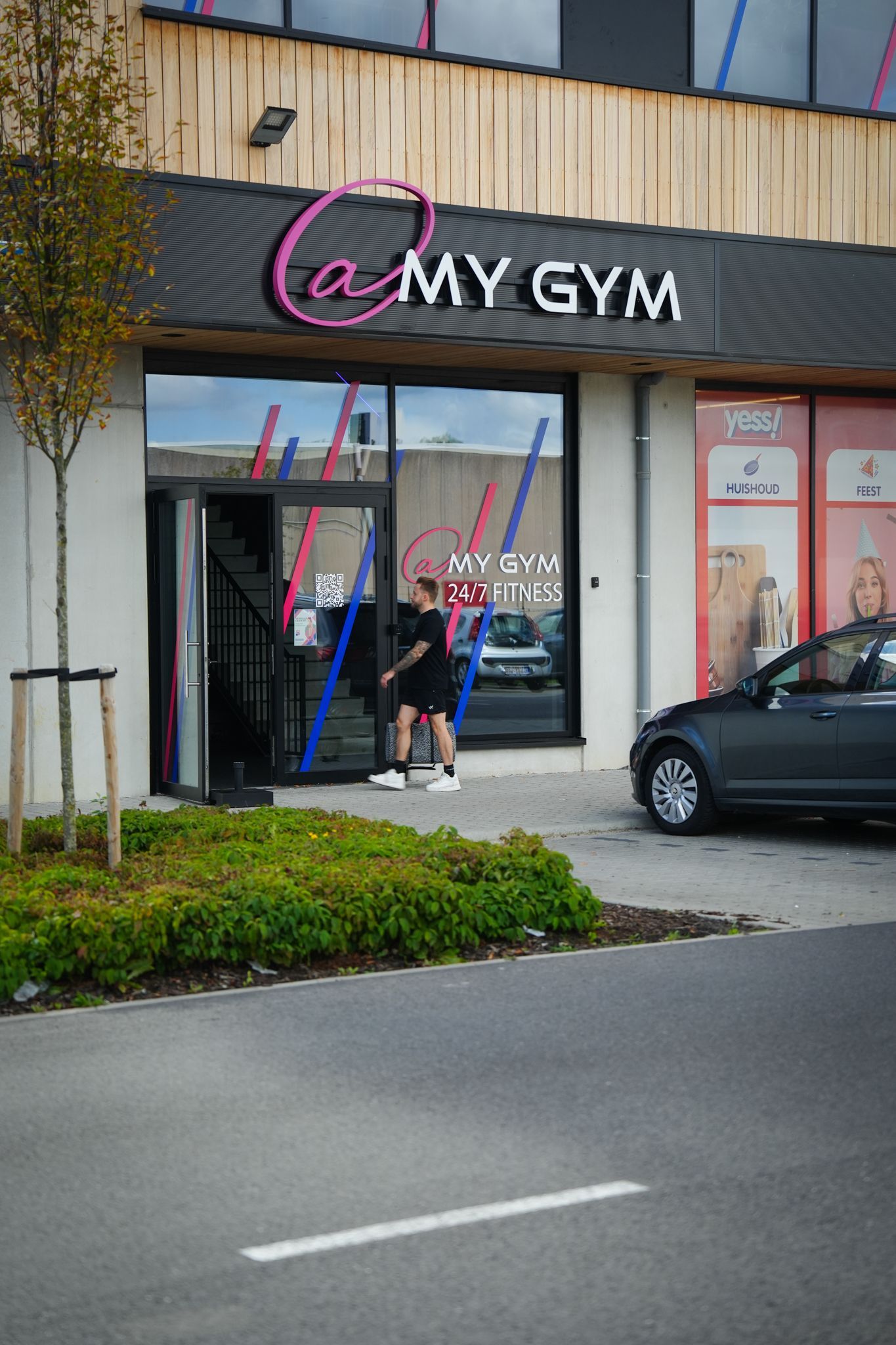 Exterior of a MY GYM storefront with a person standing at the entrance and a car parked nearby