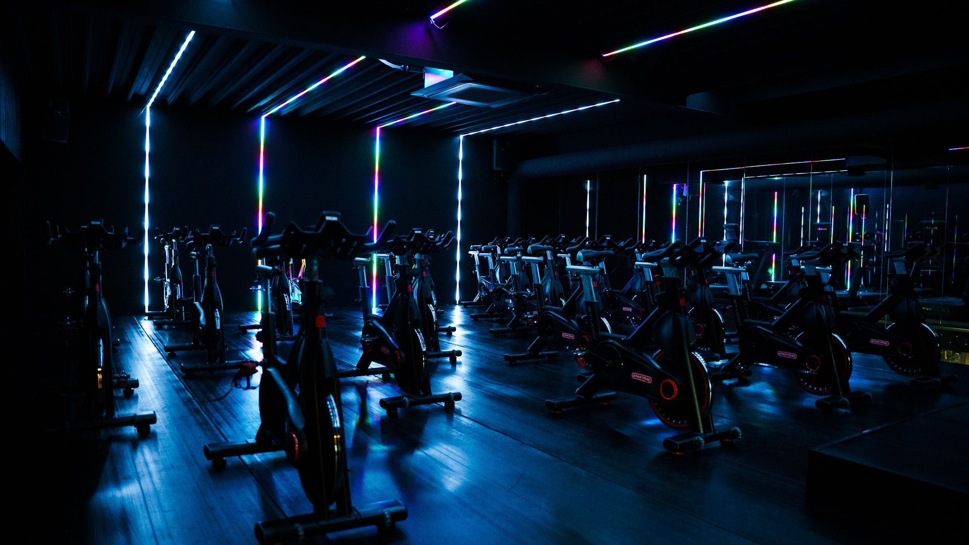 Dark gym interior with rows of exercise bikes and neon blue-purple lighting