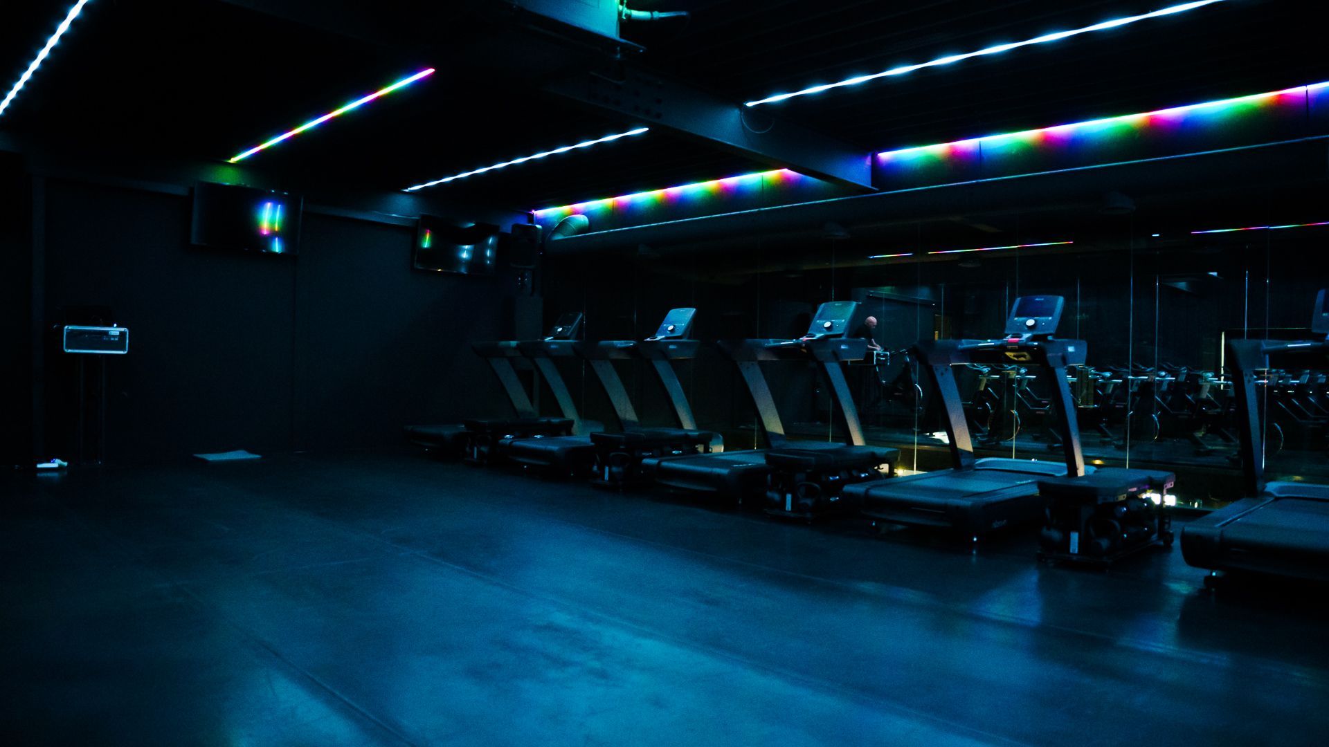Dark gym with rows of treadmills lit by blue and purple neon lights