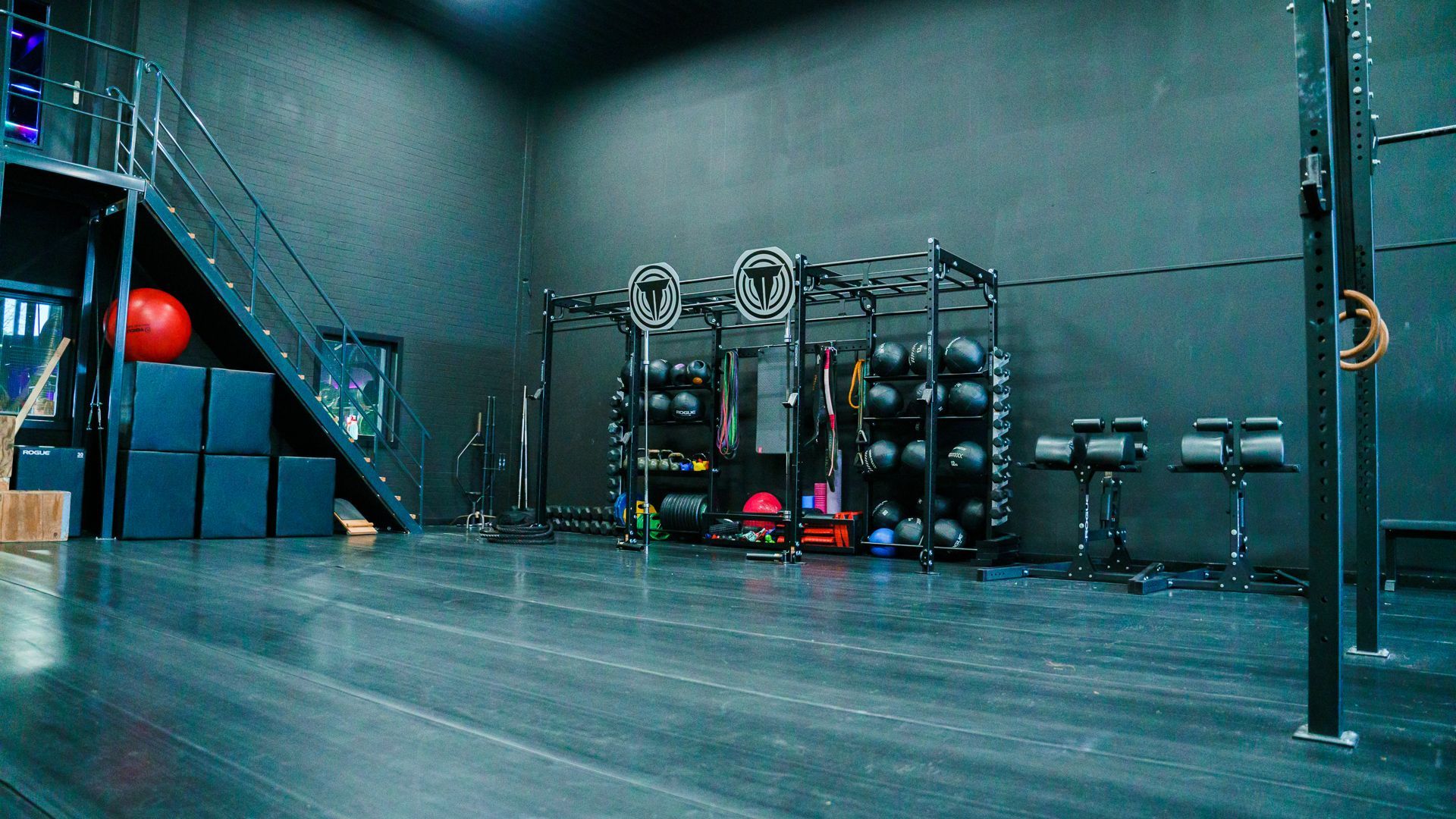 Gym with racks, barbells, and colorful weights on a polished floor under cool blue lighting