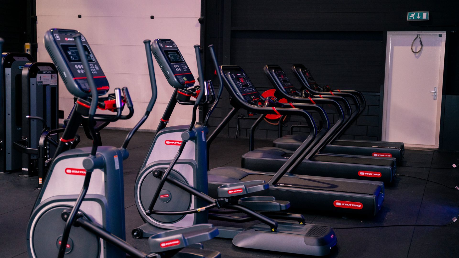 Row of treadmills and elliptical machines in a dimly lit gym workout room