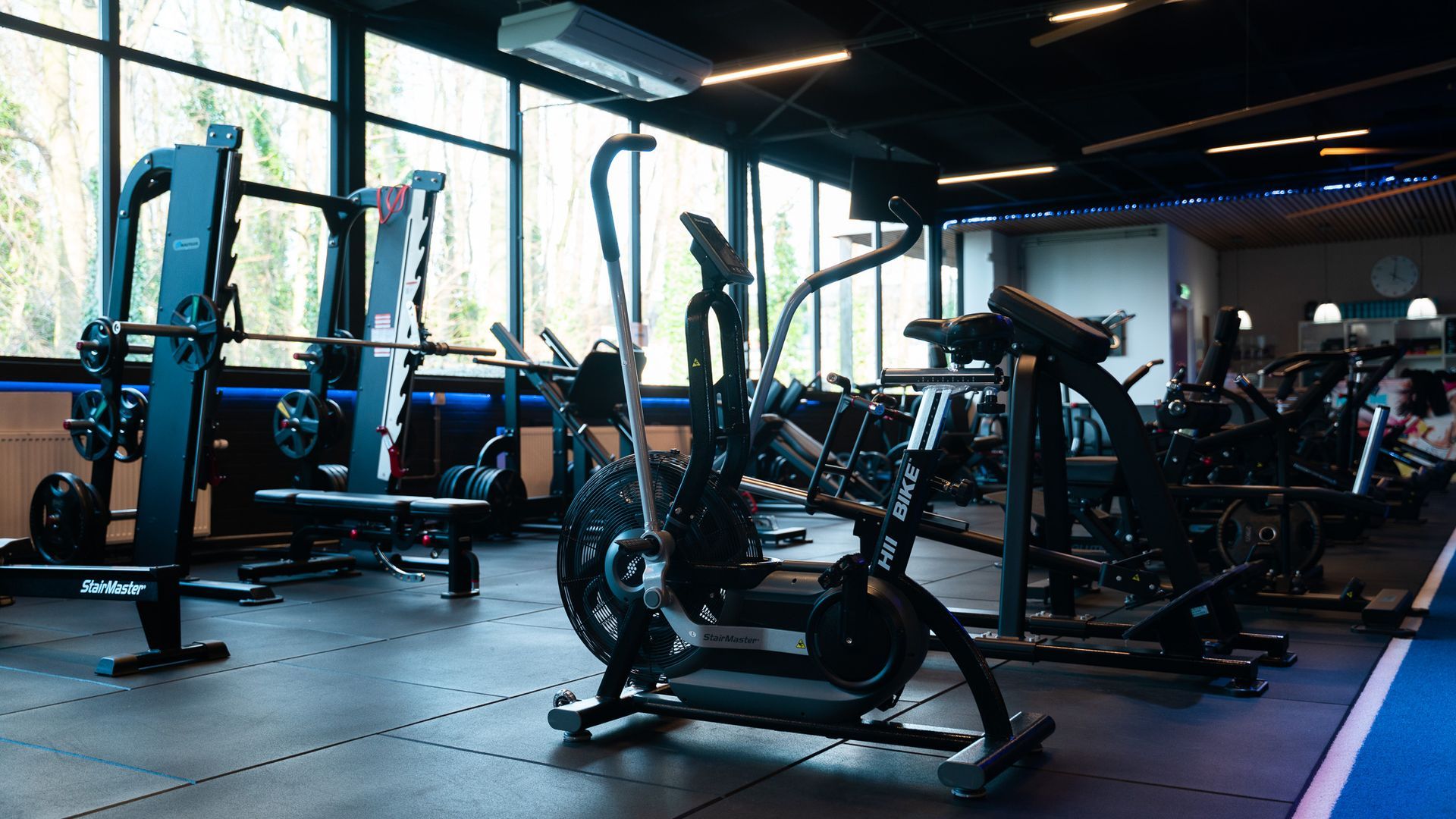 Modern gym interior with rows of exercise bikes and strength machines under blue lighting