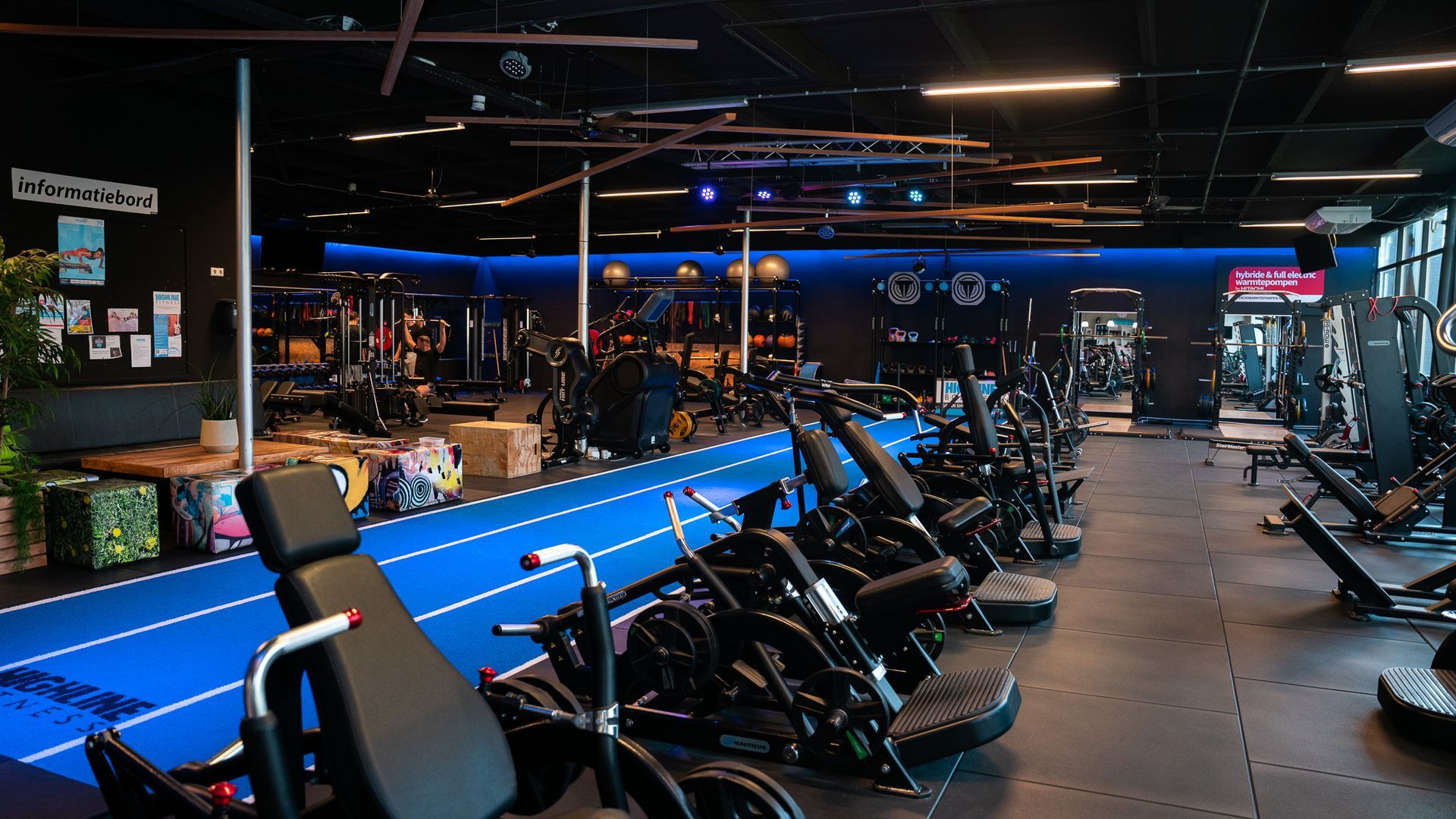 Modern gym interior with blue-lit exercise machines and treadmills in rows