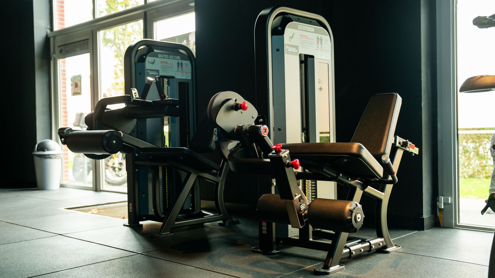 Modern gym with black exercise machines by large windows and glass doors