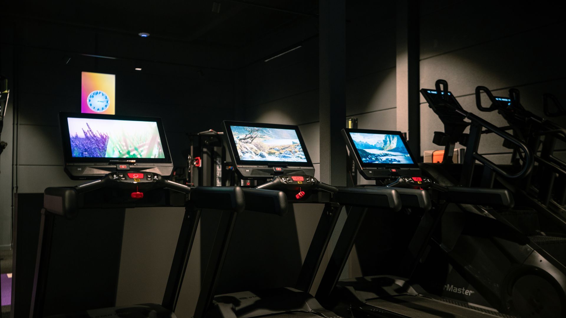 Three lit treadmills with tablet screens in a dark gym