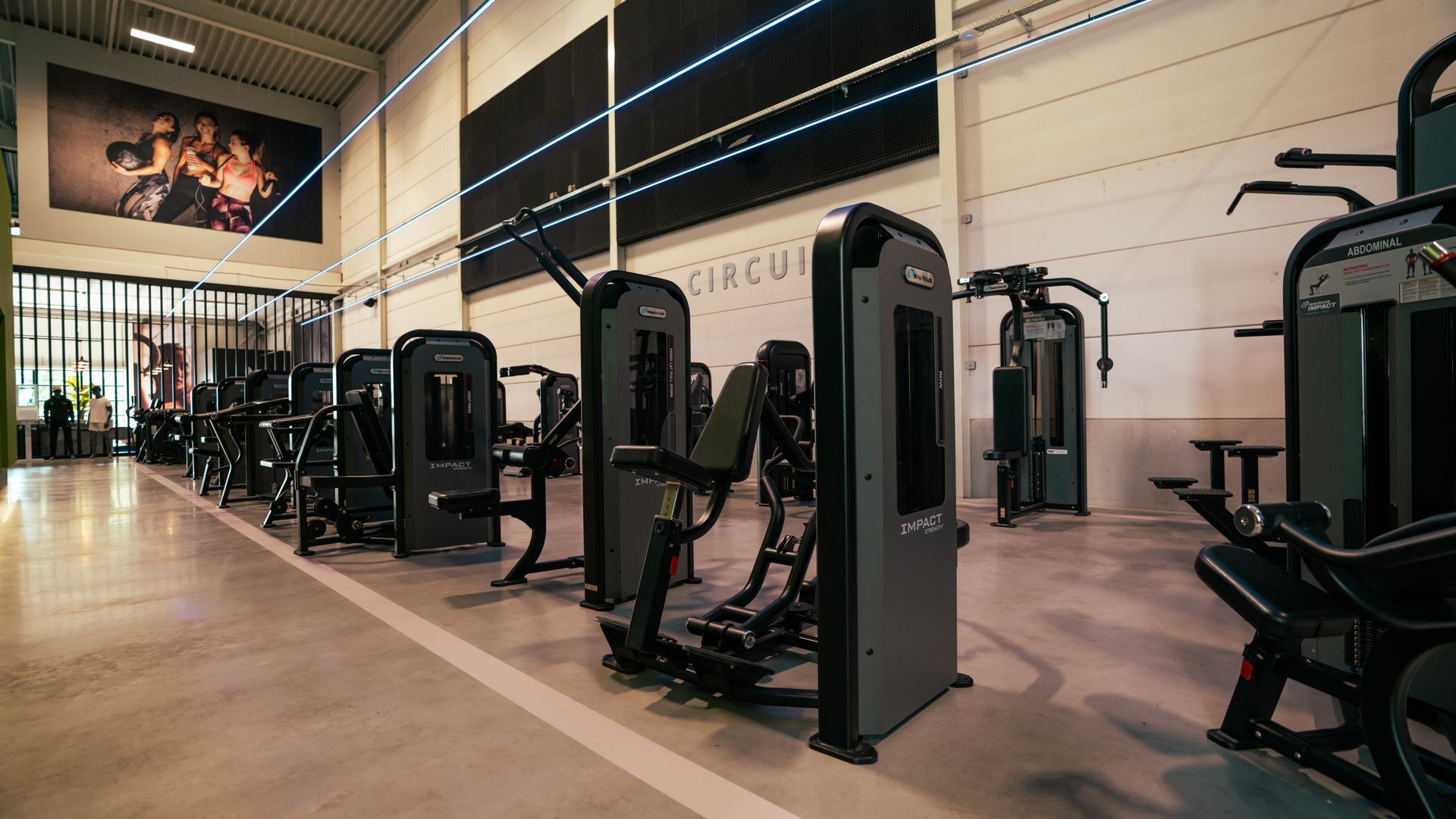 Modern gym interior with rows of strength-training machines and a wall mural under high ceilings