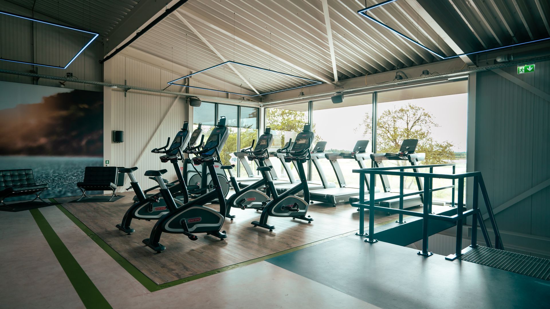 Empty modern gym with exercise bikes, treadmills, and a corrugated metal roof