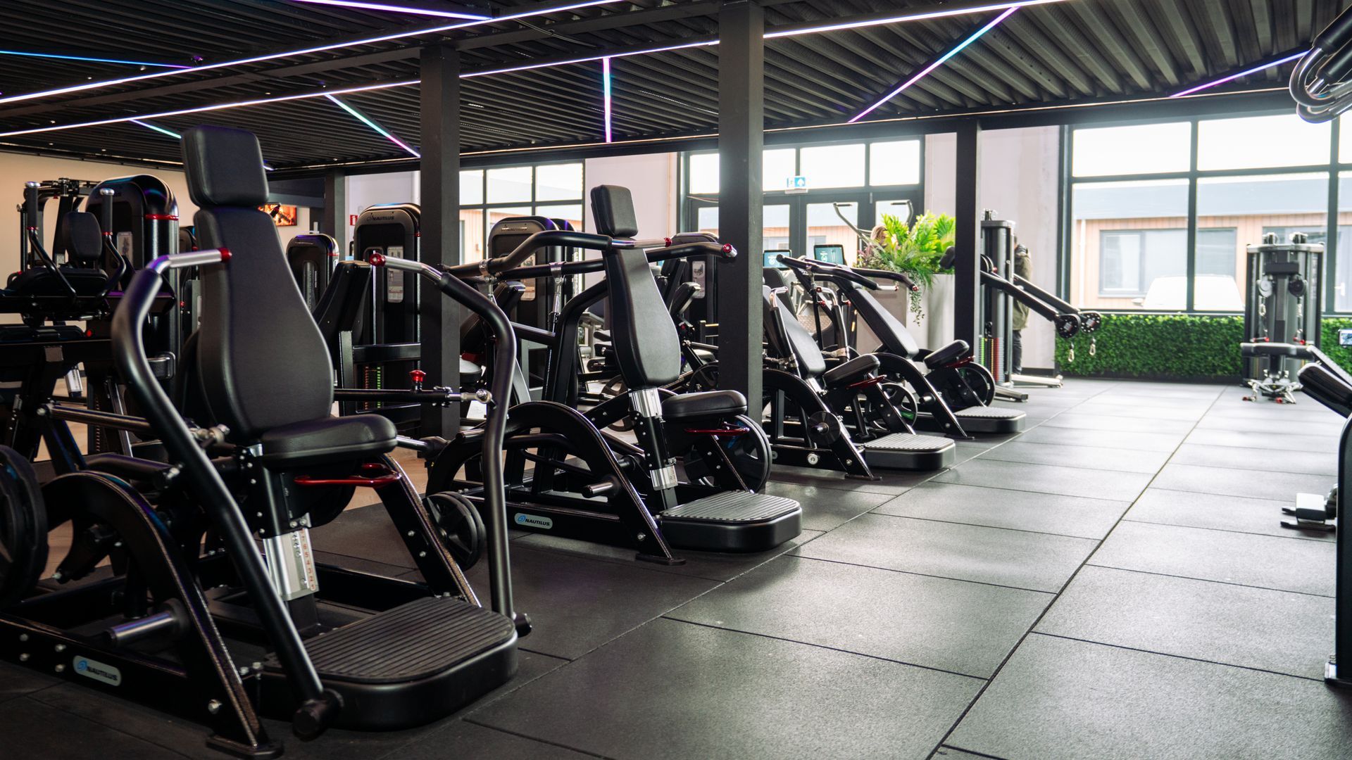 Modern gym with rows of exercise machines, black flooring, and large windows