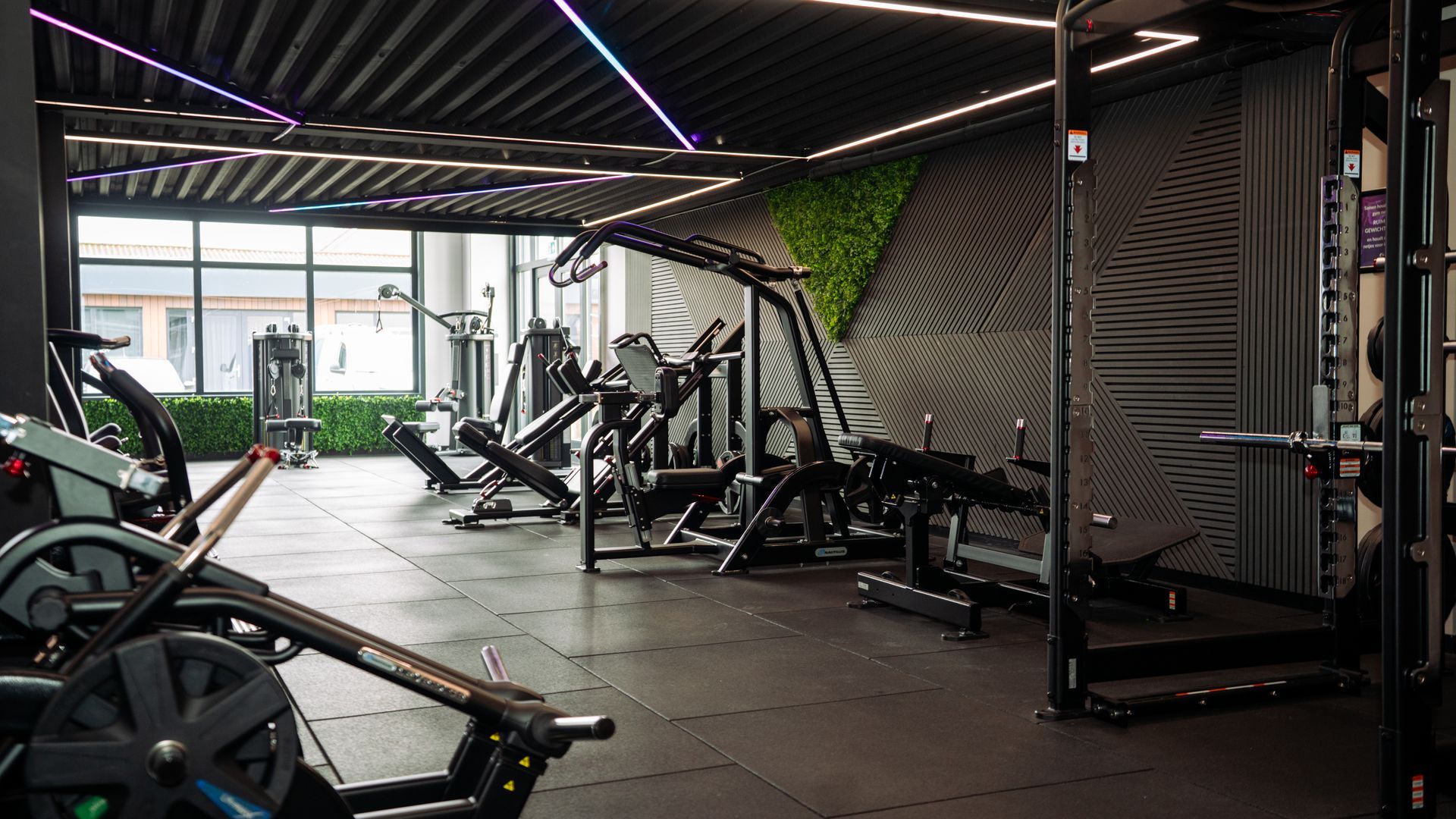 Modern gym interior with exercise machines, black flooring, and purple LED ceiling lights