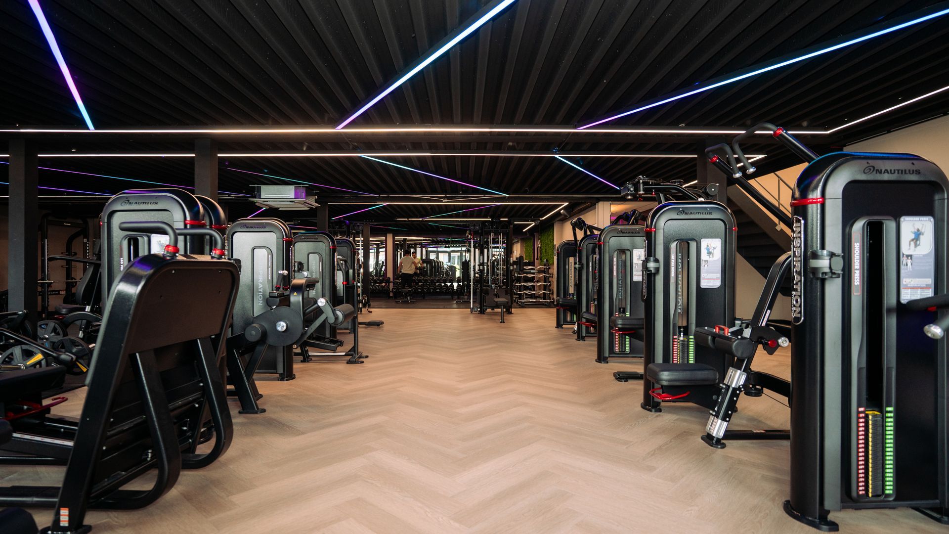 Modern gym interior with rows of exercise machines, dark decor, and LED strip lighting
