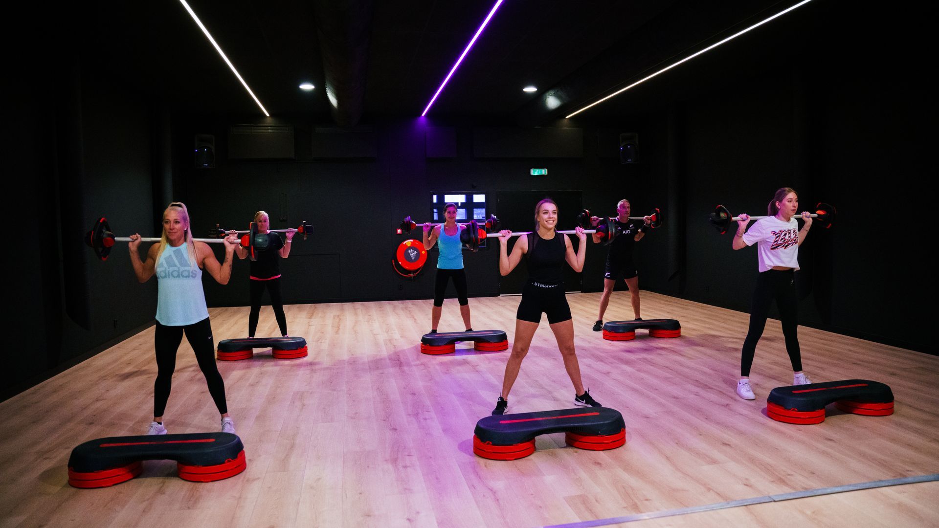 Group fitness class in a studio, people exercising on step platforms under purple lights