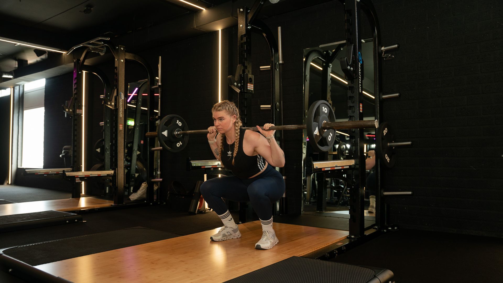 Person crouching with a barbell in a dimly lit gym, preparing to lift on a wooden platform.