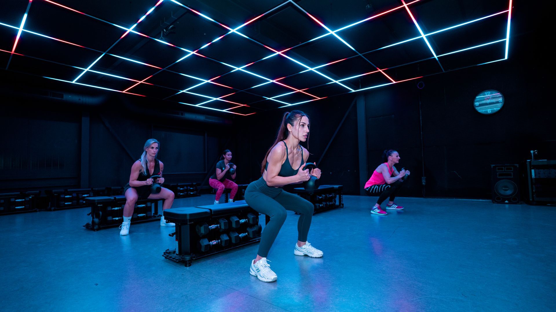 People doing a fitness class in a neon-lit gym with blue lighting and black benches