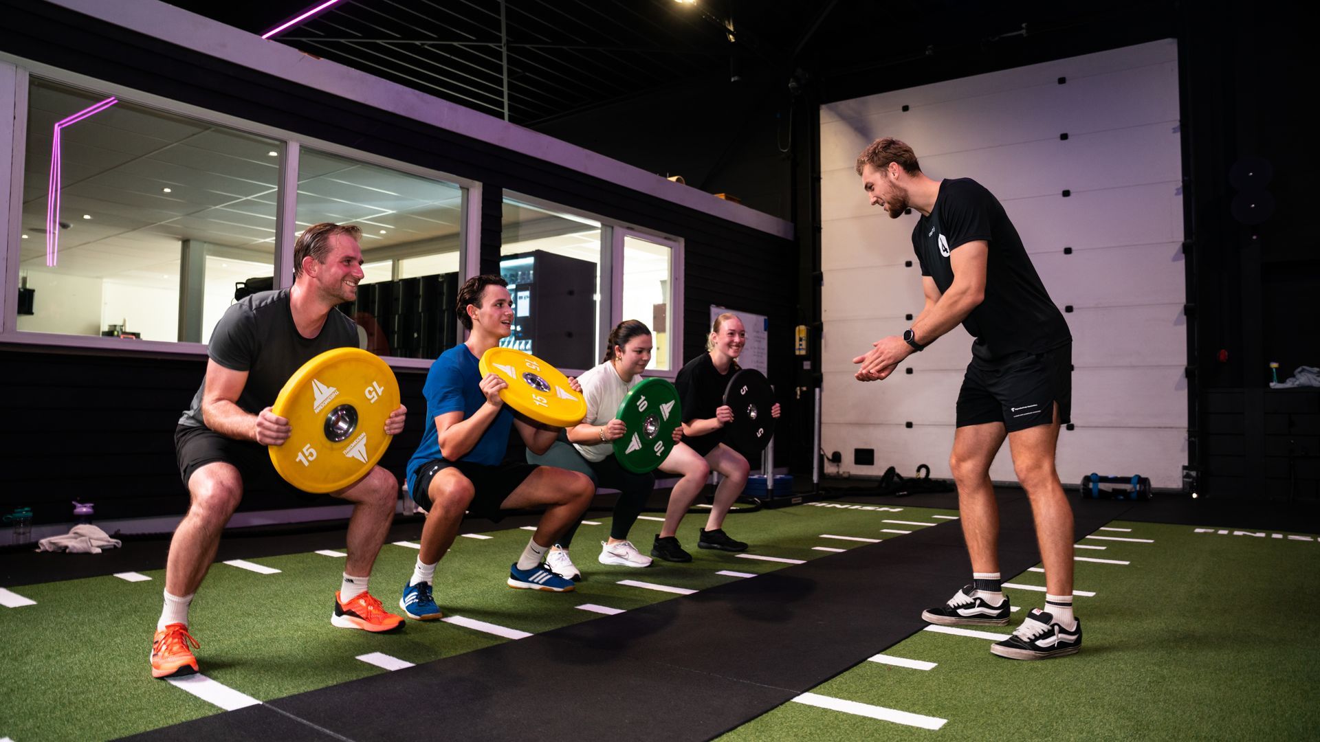 Trainer coaching athletes lifting weights in a gym with turf flooring