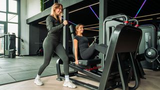 Two women exercising on a leg press machine in a modern gym.