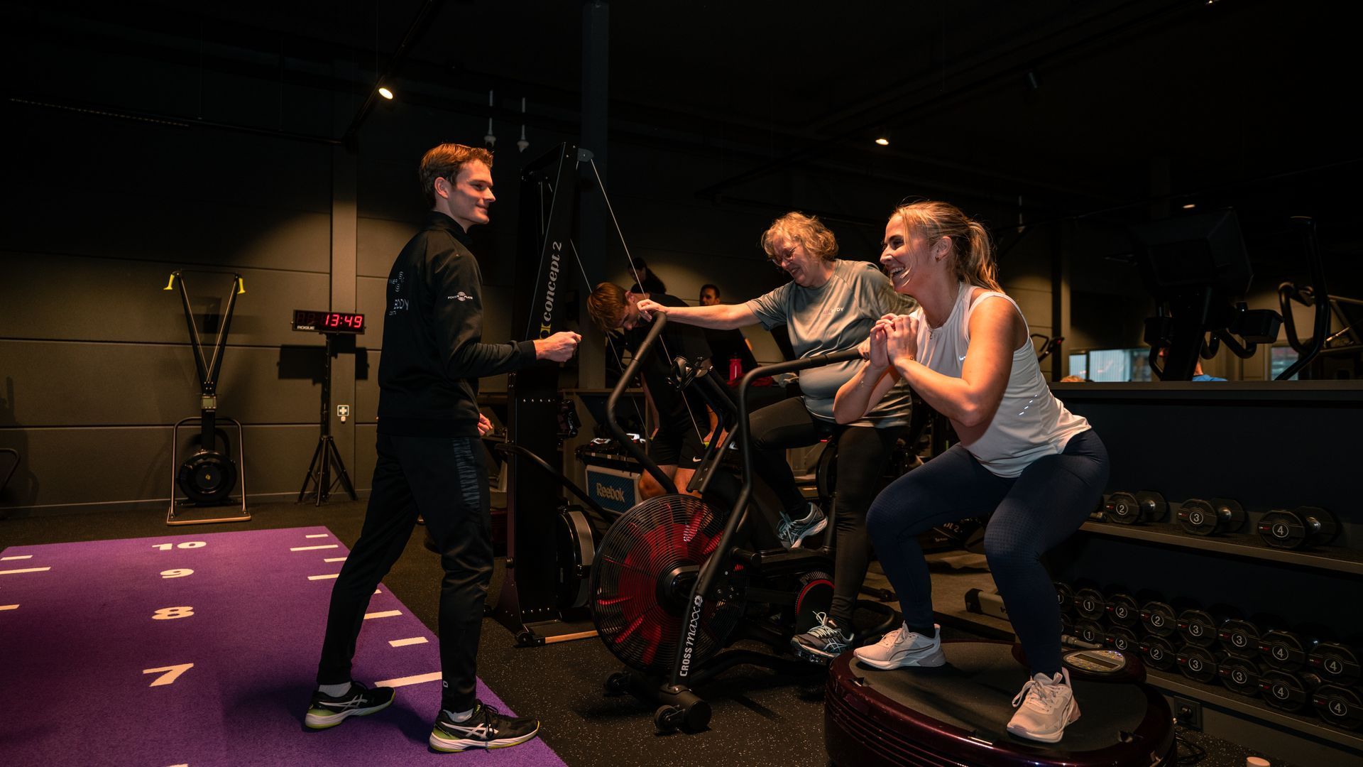 People on a dimly lit stage playing a dance game, reaching toward a central screen.