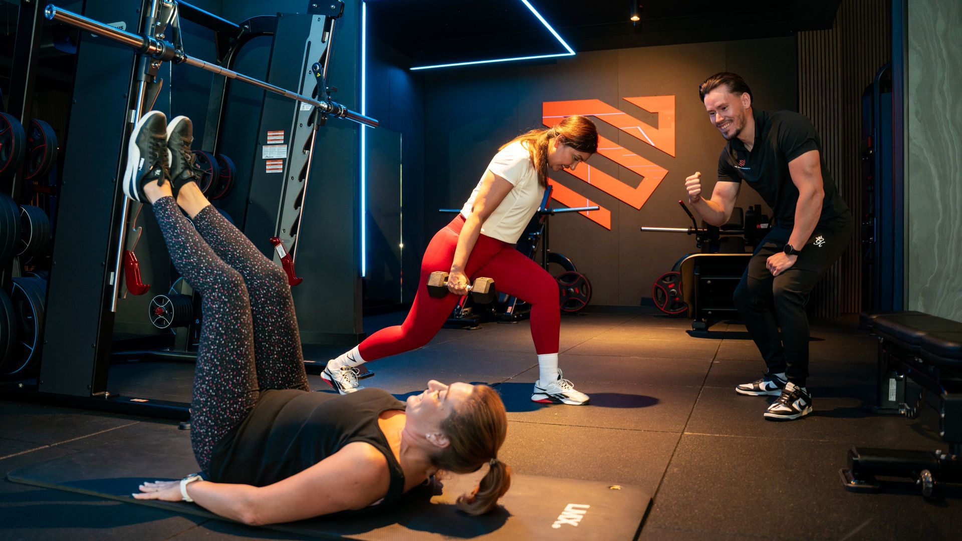 People exercising in a neon-lit gym, doing stretches and yoga poses on mats.