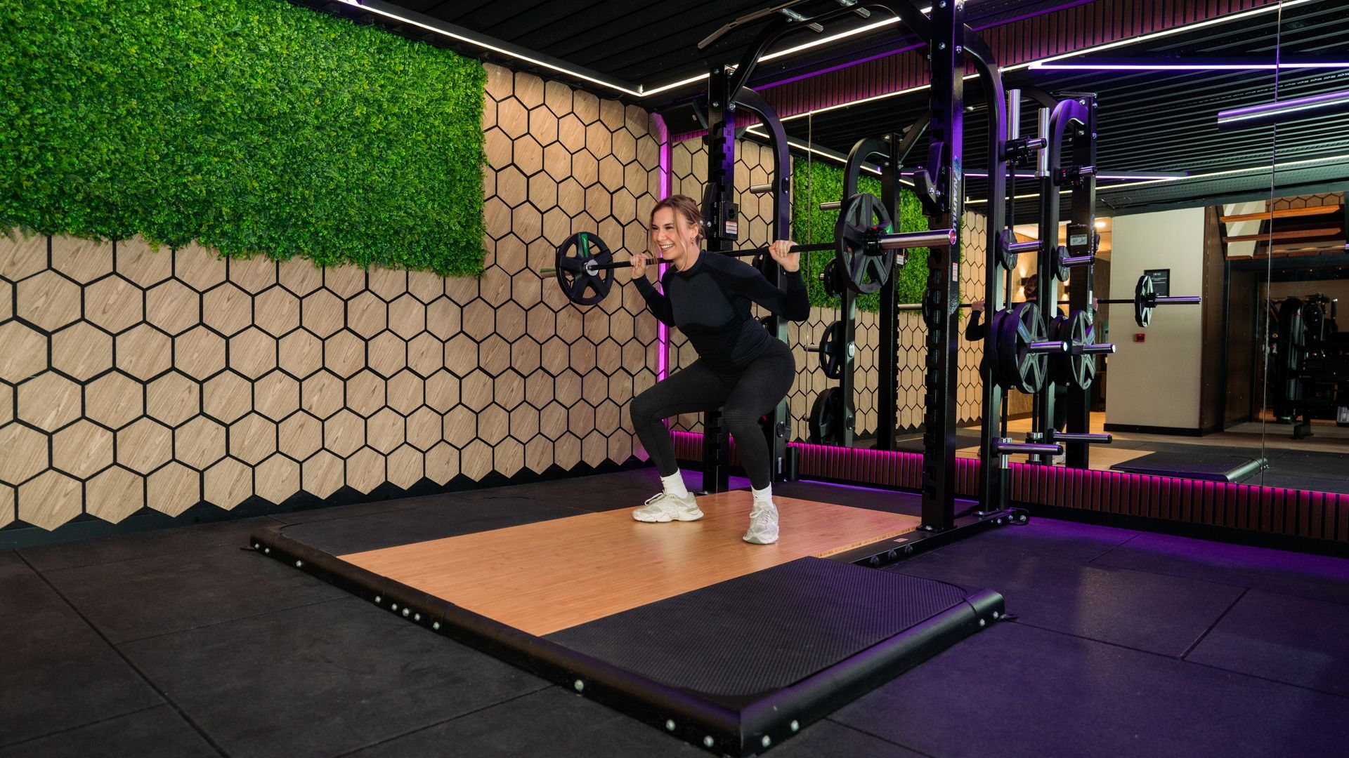 Person doing a squat exercise in a gym with purple lighting and padded floor.
