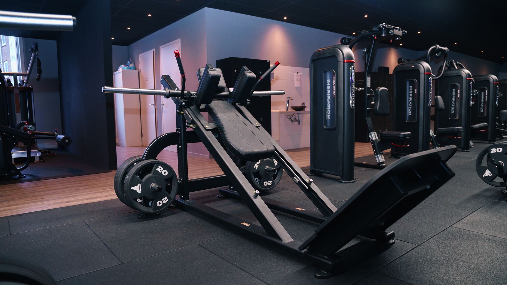 Incline leg press machine in a modern gym with black equipment and blue-purple lighting
