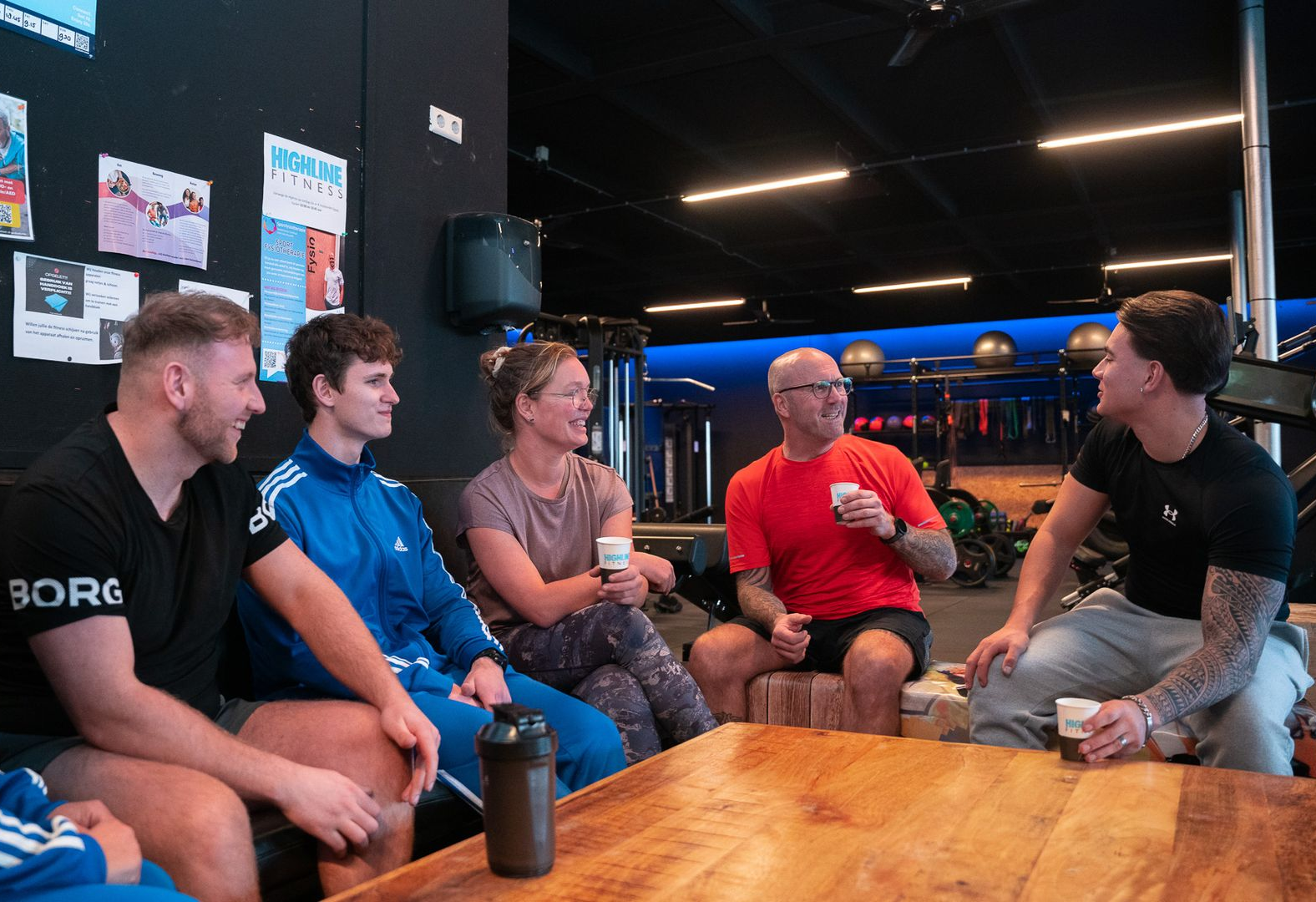 Five colleagues sit around a wooden table in an office for a collaborative meeting, discussing work with laptops and notes.
