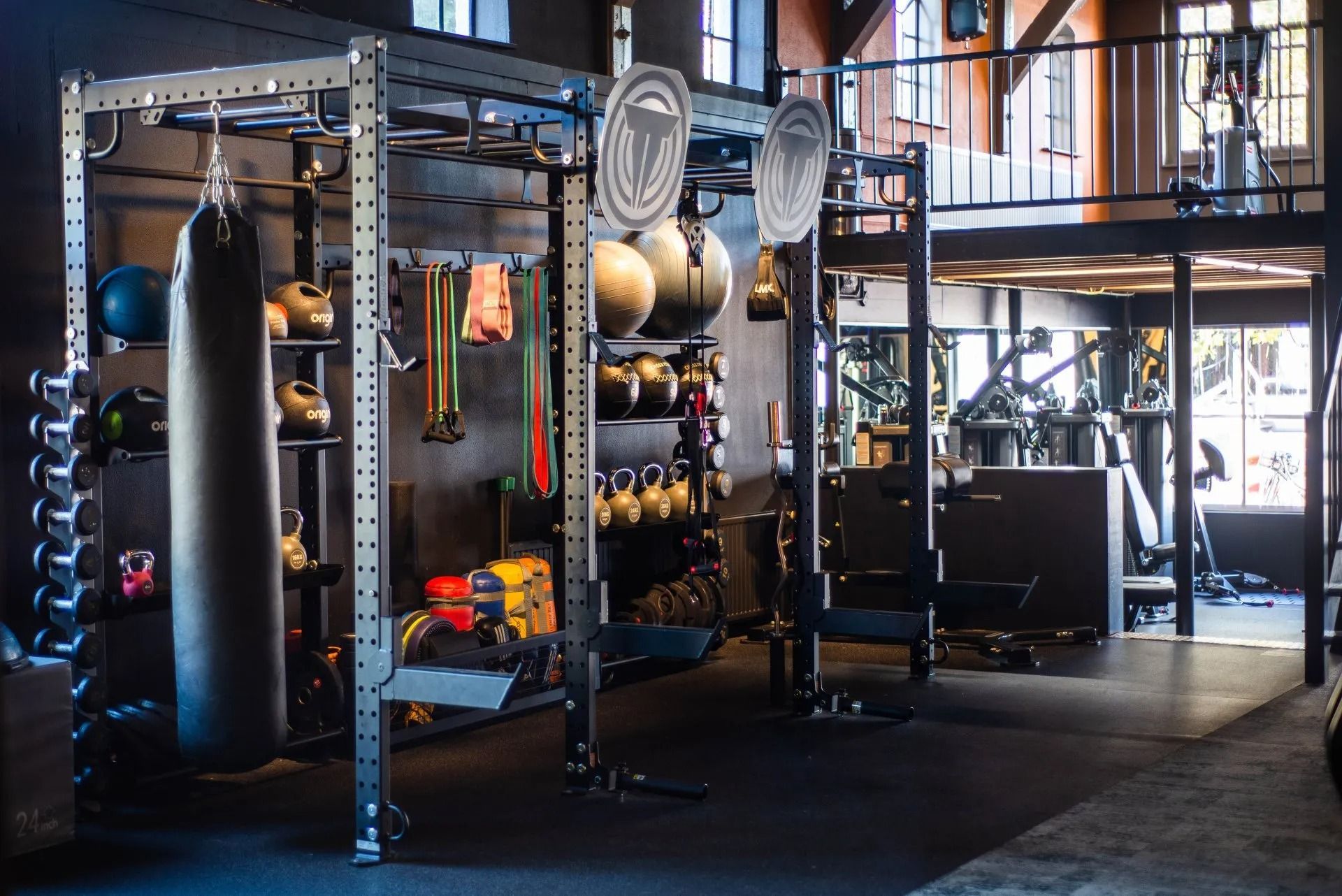 Industrial gym with metal racks, hanging punching bags, and exercise equipment in a dimly lit loft space