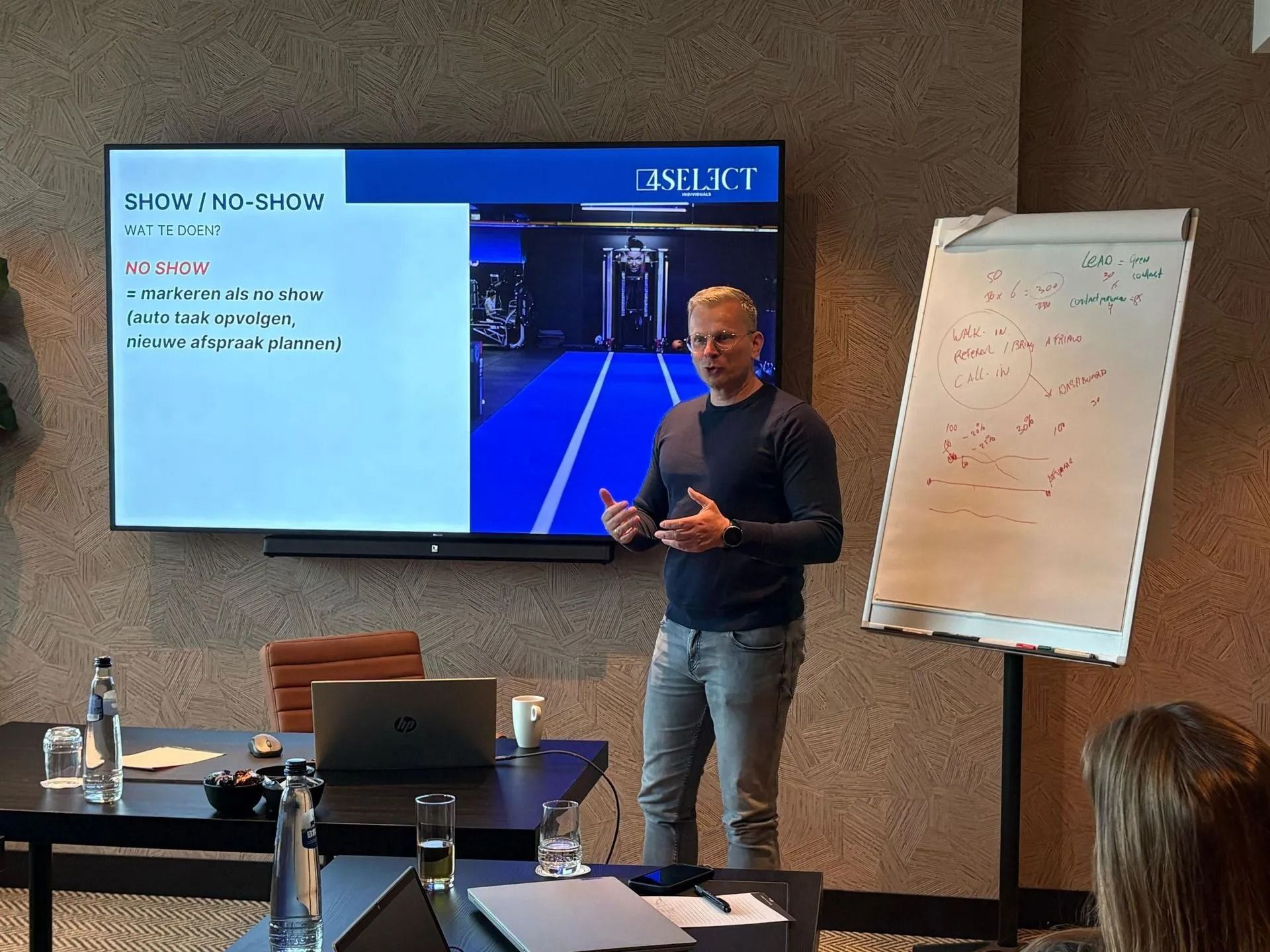 Presenter speaking beside a slide screen and whiteboard in a conference room