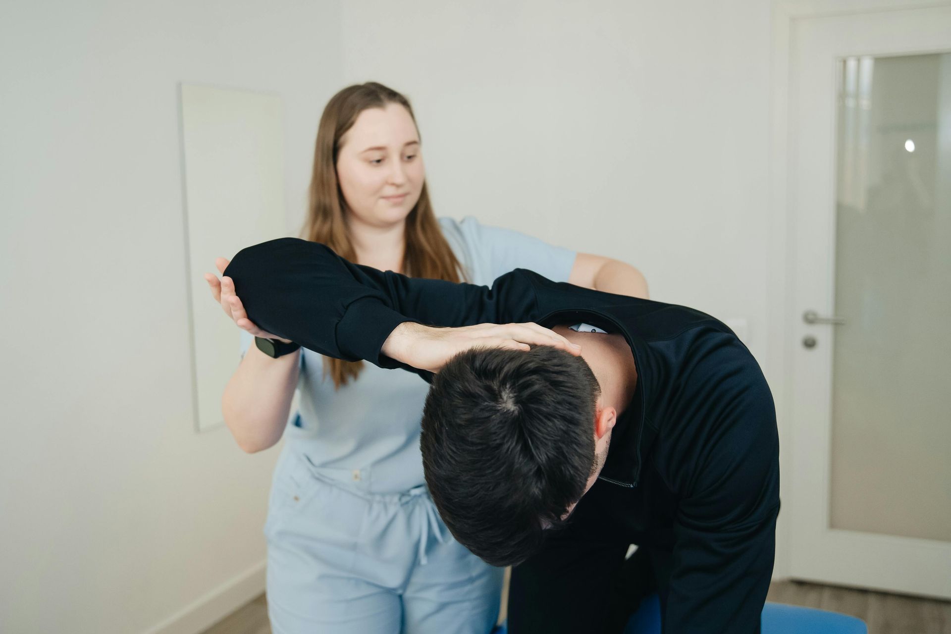 Physical therapist assisting a patient with a neck stretch in a clinic room